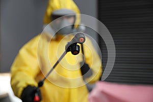 Pest control worker in protective suit, focus on insecticide sprayer