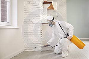 Pest control worker in protective suit spraying cockroach insecticide in the kitchen