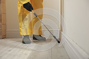 Pest control worker in protective suit spraying insecticide on floor indoors