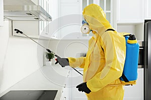 Pest control worker in protective suit spraying insecticide on furniture