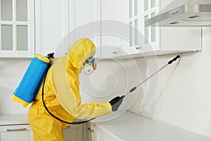 Pest control worker in protective suit spraying insecticide on furniture