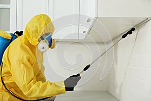 Pest control worker in protective suit spraying insecticide on furniture