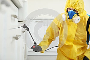 Pest control worker in protective suit spraying insecticide on furniture