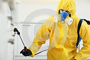 Pest control worker in protective suit spraying insecticide on furniture