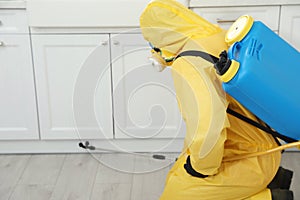 Pest control worker in protective suit spraying insecticide on furniture. Space for text