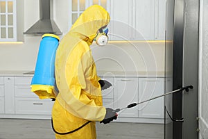 Pest control worker in protective suit spraying insecticide near refrigerator