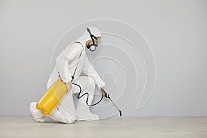 Pest control worker in protective suit spraying insecticide to clean house from insects