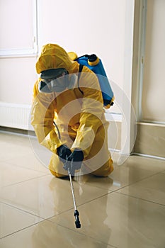 Pest control worker in protective suit spraying pesticide