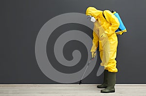 Pest control worker in protective suit spraying pesticide near black wall. Space for text