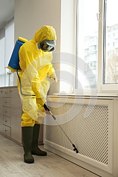 Pest control worker in protective suit spraying pesticide near window