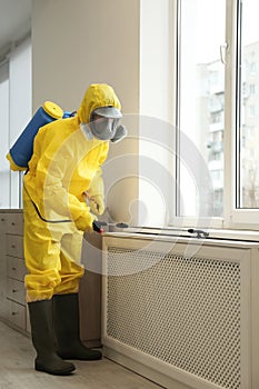 Pest control worker in protective suit spraying pesticide near window