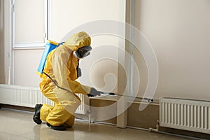 Pest control worker in protective suit spraying pesticide. Space for text