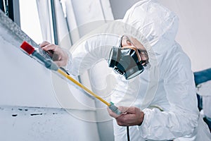 pest control worker in respirator spraying pesticides under windowsill