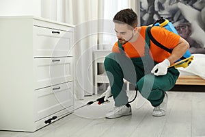 Pest control worker spraying insecticide near chest of drawers