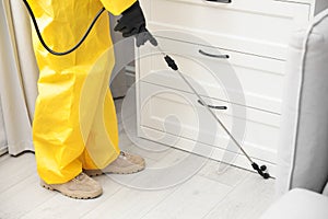 Pest control worker spraying pesticide around furniture indoors