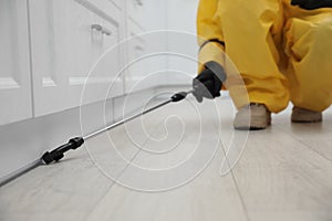 Pest control worker spraying pesticide around furniture indoors