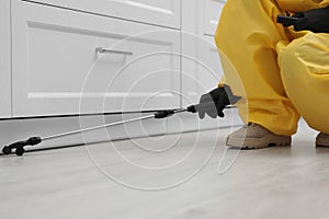 Pest control worker spraying pesticide around furniture indoors