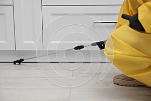 Pest control worker spraying pesticide around furniture indoors, closeup