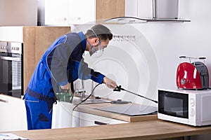 Pest Control Worker Spraying Pesticide In Kitchen