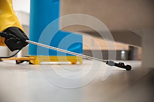 Pest control worker spraying pesticide under furniture, closeup