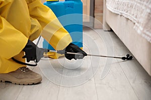 Pest control worker spraying pesticide under furniture indoors