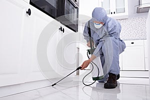 Pest Control Worker Spraying Pesticide On White Cabinet