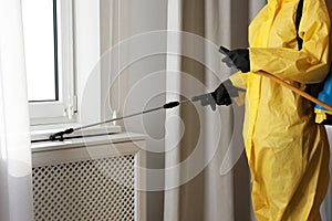 Pest control worker spraying pesticide on window sill indoors