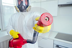 Pest control worker standing with sprayer in kitchen