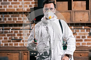 pest control worker standing with sprayer in kitchen and looking
