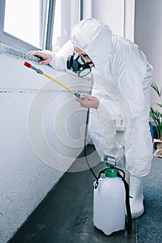 pest control worker in uniform spraying pesticides under windowsill