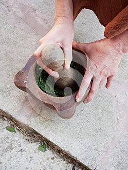 pestle pounding leaves in a big wooden mortar