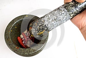 Pestle in woman hand above the mortar with chilli and garlic ins