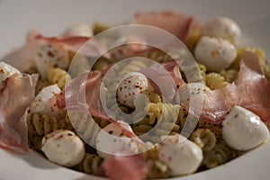 Pesto fusilli with mozzarella and coppa ham on white plate
