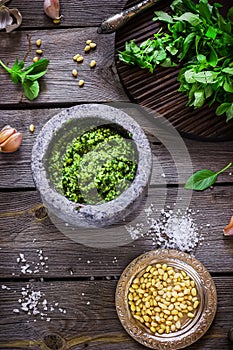 Pesto in marble mortar, salt, pine nuta and garlic on wooden table. photo