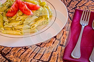 Pesto penne pasta with fresh tomatoes and iced tea on a tree stump background.