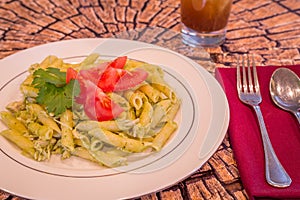 Pesto penne pasta with fresh tomatoes and iced tea on a tree stump background.