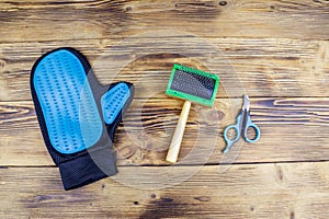 Pet accessories on wood background. Blue rubber grooming glove, pet slicker brush and claw clipper on wooden background