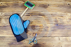 Pet accessories on wood background. Blue rubber grooming glove, pet slicker brush and claw clipper on wooden background