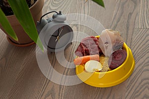 Pet care and diet concept. Bowl of raw food with meat, fish and vegetables on wooden background. Feed on time concept