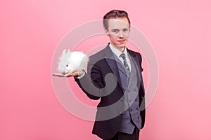 Pet care. Portrait of young handsome positive man in elegant suit holding rabbit on his palm. indoor studio shot isolated on pink