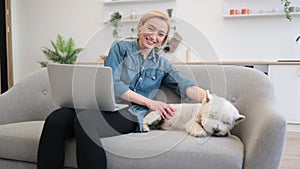 Pet owner with laptop fondling dog on kitchen couch