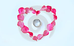 Petals of rose flower in heart shape with couple wedding rings on white background