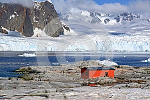 Petermann Island, beautiful Antarctic Island with penguins on rocks, abandoned station and snow covered mountains behind Ocean.