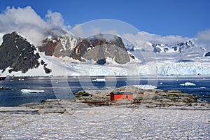 Petermann Island, beautiful Antarctic Island with penguins on rocks, abandoned station and snow covered mountains behind Ocean.