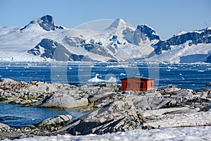 Petermann Island, beautiful Antarctic Island with penguins on rocks, abandoned station and snow covered mountains behind Ocean.