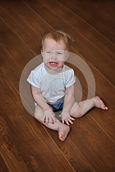 Petite crying baby girl sitting indoor on the wooden floor