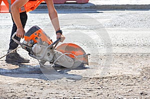 A petrol disc cutter in the hands of a worker cuts the asphalt concrete road surface on a sunny summer day