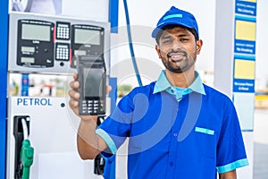 Petrol pump worker showing swiping machine by looking camera at fuel station - concept of digital payment, cashless