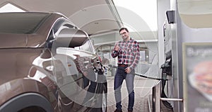 Petrol station, auto fueling concept. Portrait of young handsome Caucasian man standing outdoors at gas station and