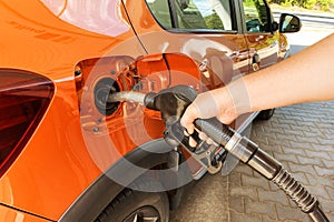 Petrol station pump. Pumping gasoline fuel in orange car at a gas station. Fill orange car with fuel in petrol station. Sunlight